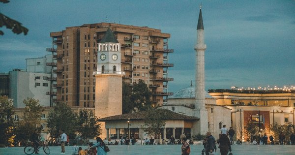 People crossing a plaza in central Tirana with the historic clock tower and minaret rising in the background