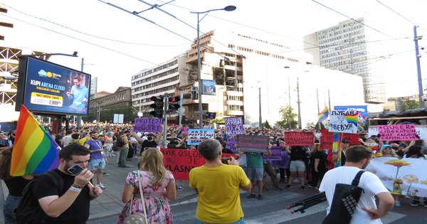 A Pride march moving through a city street with rainbow flags