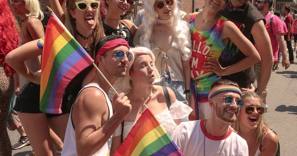 A large Pride crowd with rainbow flags on a city street