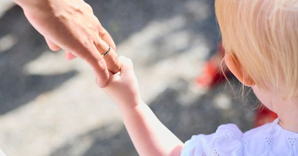 Two parents holding a small child's hands while walking outdoors, seen from behind.