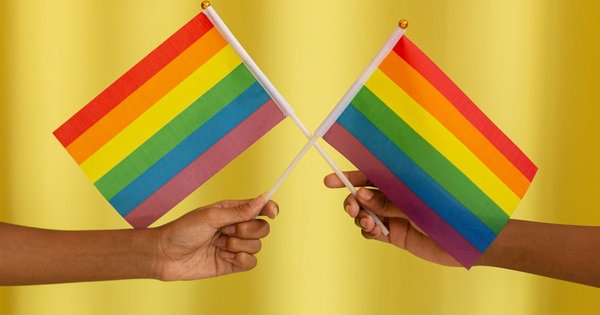 Two hands holding crossed rainbow pride flags