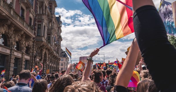 A crowd of Pride marchers waving rainbow flags on a city street
