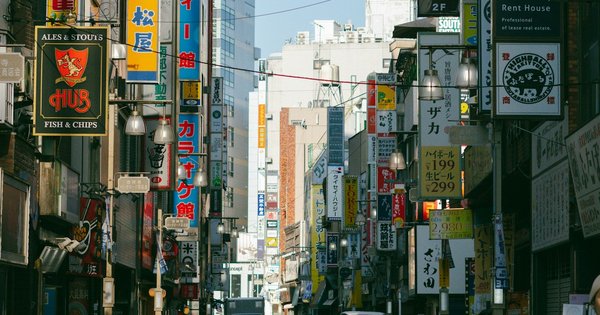 A street in Tokyo with a Pride flag visible among pedestrians