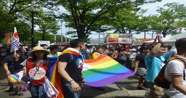 A rainbow flag held aloft against a sunny sky at Tokyo Rainbow Pride