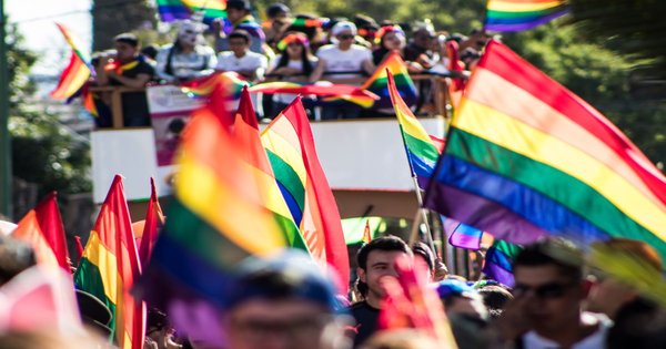 A large rainbow pride flag carried through a street march in Latin America