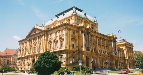 The Croatian National Theatre in central Zagreb, a yellow neo-baroque building under a clear blue sky.