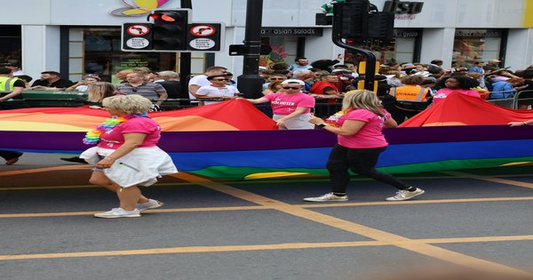 A crowd of marchers carrying a large rainbow Pride flag through a street