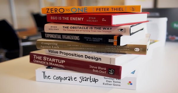 A stack of colorful books on a wooden table next to a cup of coffee