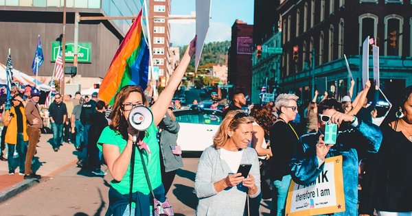 A pride protest with a rainbow flag held aloft, representing LGBTQ+ visibility under threat