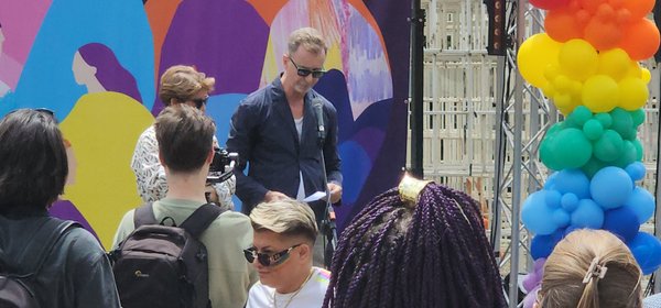 EU Ambassador Silvio Gonzato speaking at Tirana Pride 2026, standing at a microphone with a colorful mural behind him