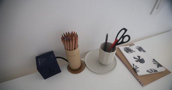 A desk with a notebook, pens and pencils in soft daylight