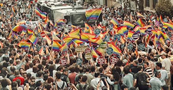 A large, dense crowd waving rainbow flags and placards at a Pride march