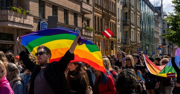 A rainbow flag held up against a Balkan city skyline