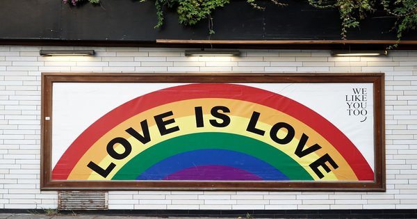 A large crowd waving rainbow and pride flags at an outdoor Pride celebration.