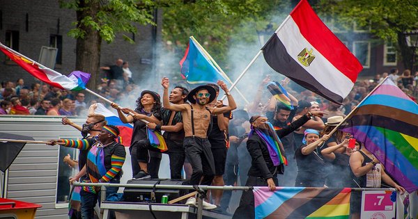 Rainbow flags flying over an Amsterdam canal lined with historic buildings during Pride