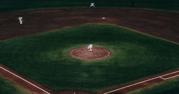 A baseball resting on the chalk of a sunlit infield with stadium lights in the background.